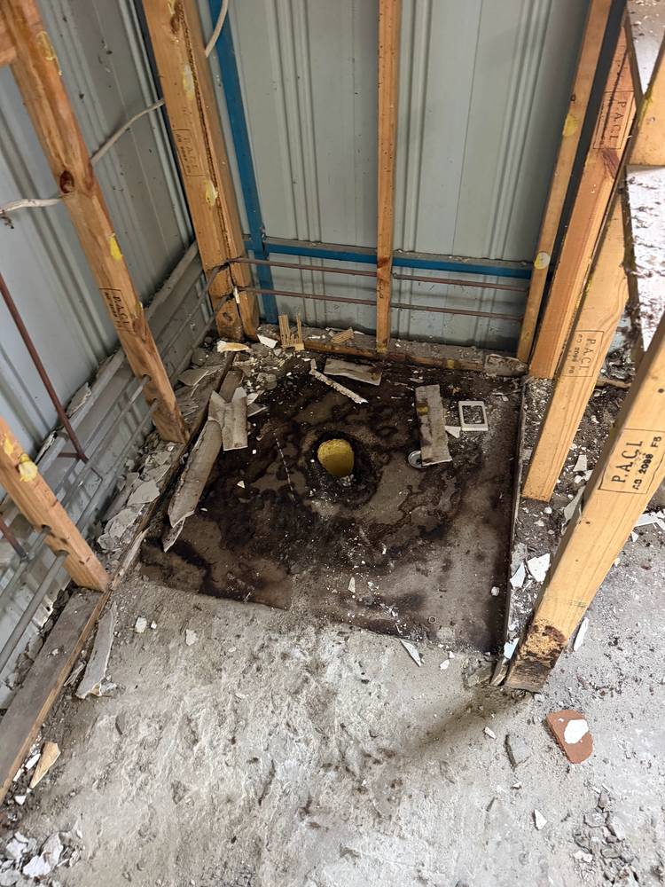 Old shower stripped back to the frame, with rubbish on the floor